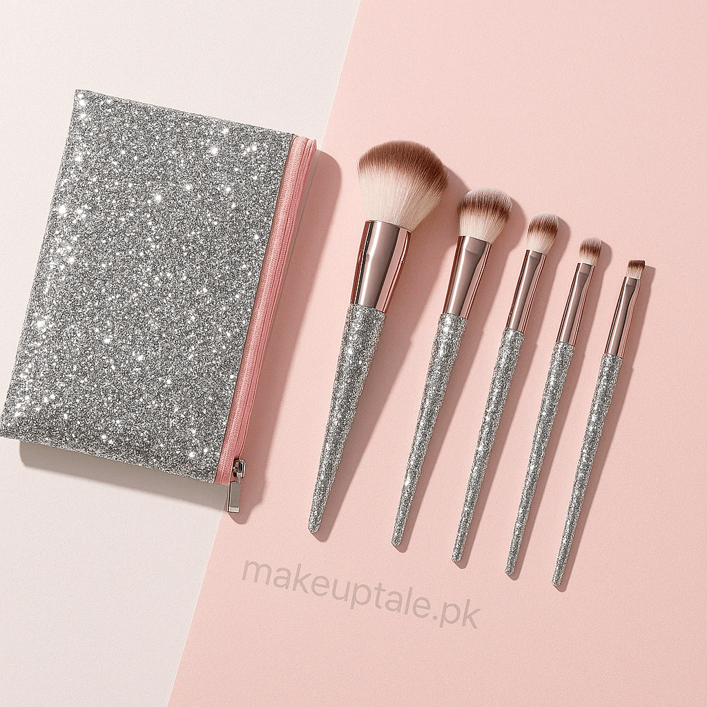 A set of five makeup brushes with glitter handles, displayed alongside a sparkling silver and pink zip pouch on a two-tone background.